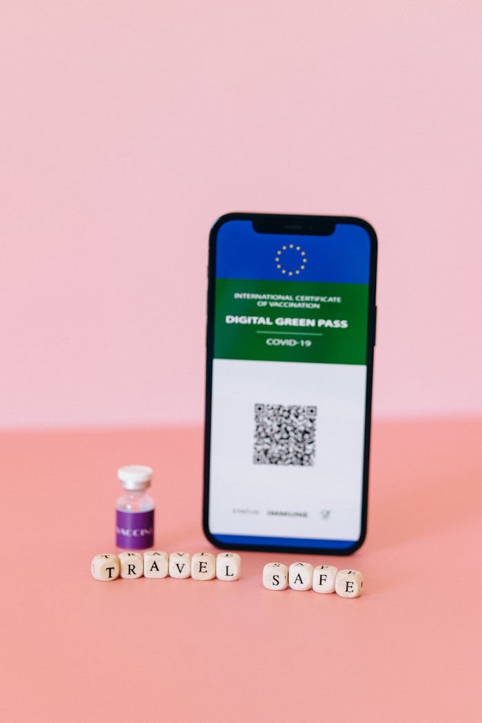 Smartphone displaying digital COVID-19 green pass with vaccine vial on pink background.